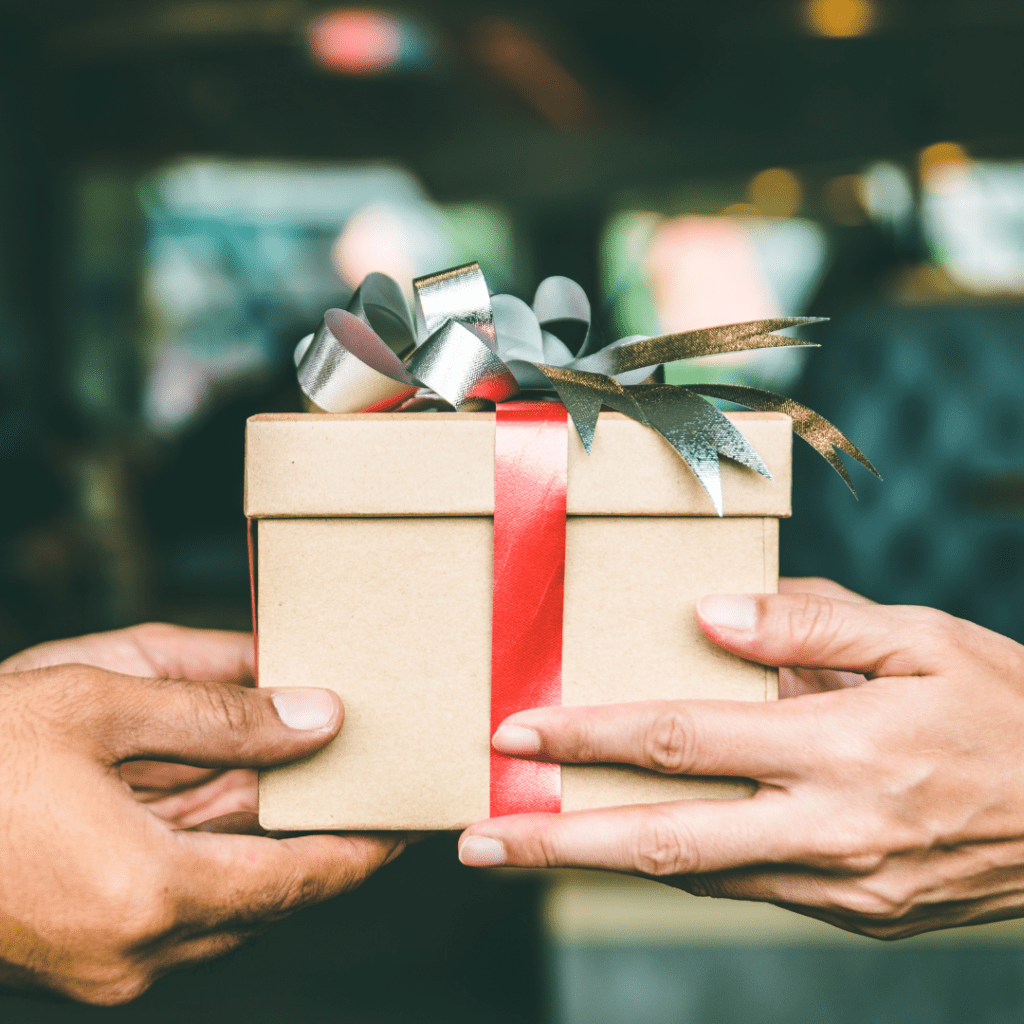 En la imagen se observan dos pares de manos sosteniendo un regalo