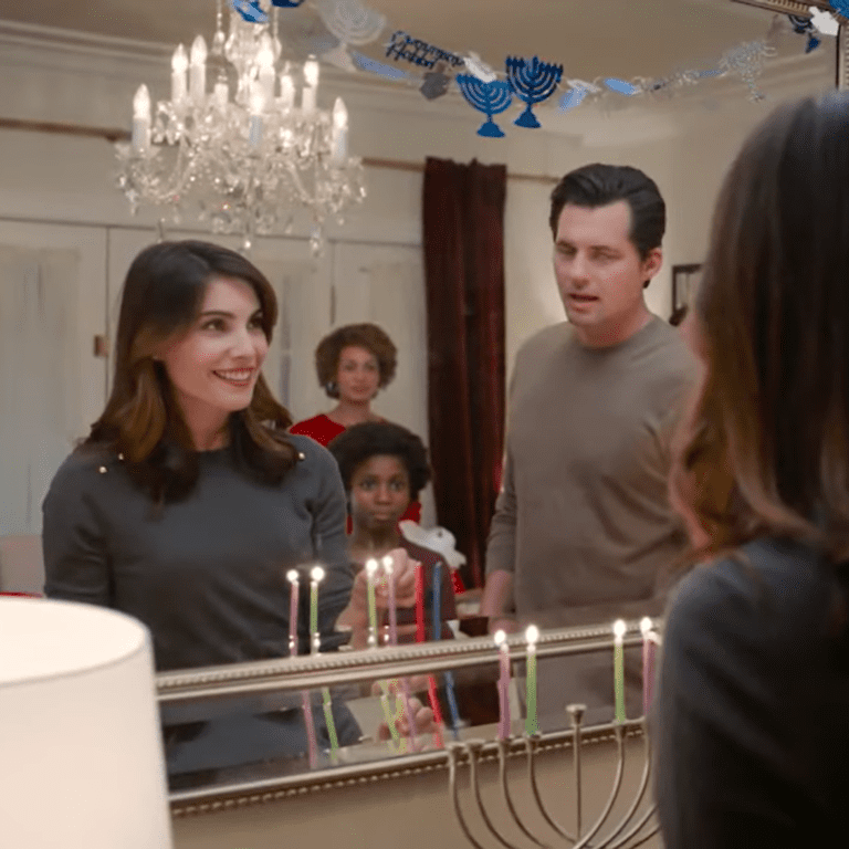 En la imagen se observa una pareja, un niño y una mujer encendiendo un Menorah frente a un espejo