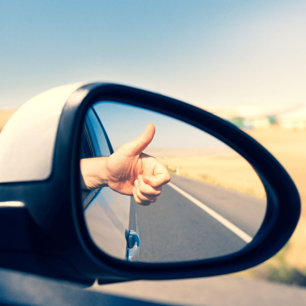 En la imagen se muestra una mano con el pulgar arriba, reflejada en un espejo retrovisor