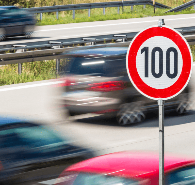 En la imagen se muestran vehículos conduciendo al rededor de un señalamiento de velocidad