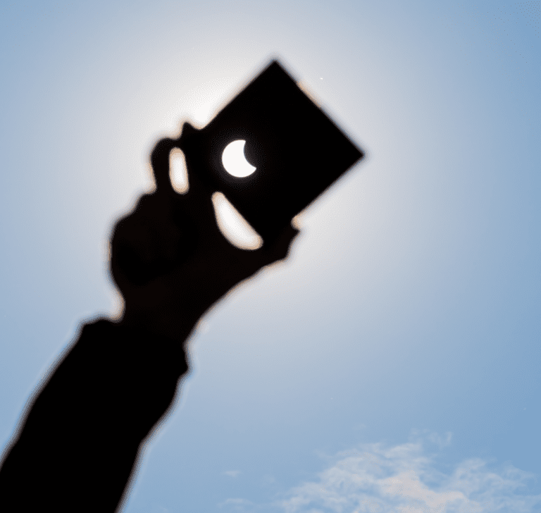 En la imagen se muestra una mano sosteniendo un cartón para ver un eclipse solar