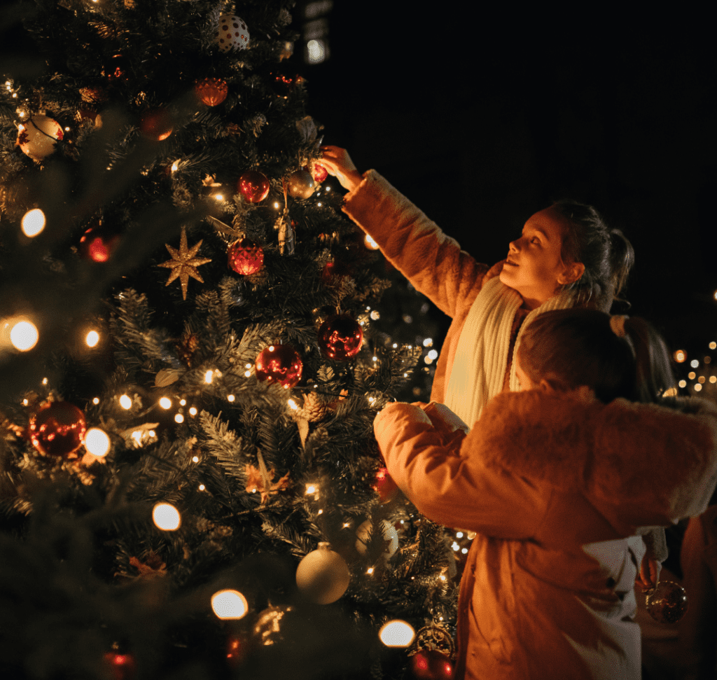 En la imagen se muestran dos niñas decorando un árbol de Navidad