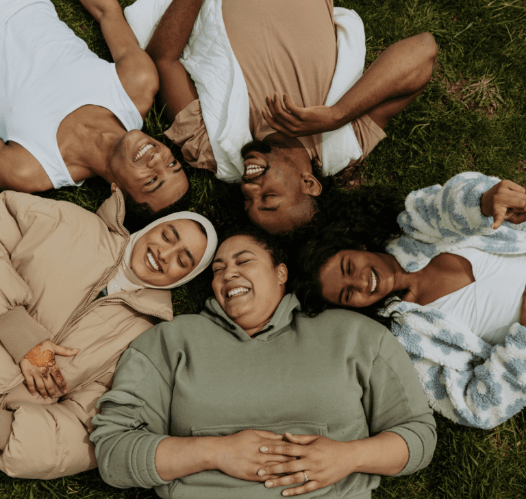 En la imagen se muestran personas sonriendo recostadas en el césped